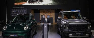 Man in suit at a podium presenting between two Haval SUVs in a showroom, with a large vehicle banner above.