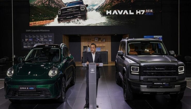 Man in suit at a podium presenting between two Haval SUVs in a showroom, with a large vehicle banner above.