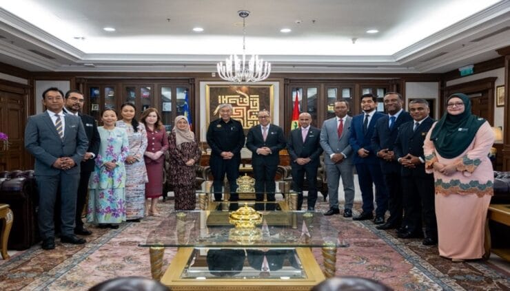 Group of professionals in formal attire posing for a photo in a wood-paneled meeting room with a chandelier and decorative rug.