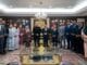 Group of professionals in formal attire posing for a photo in a wood-paneled meeting room with a chandelier and decorative rug.