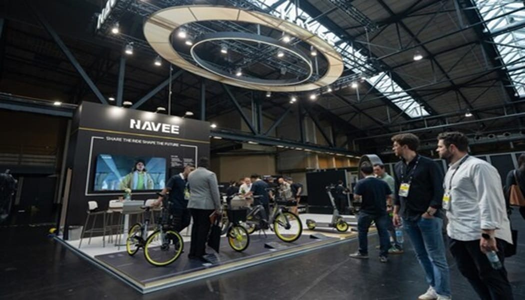 NAVEE exhibition booth at a trade show displaying electric bikes with bright yellow rims and a large screen backdrop.